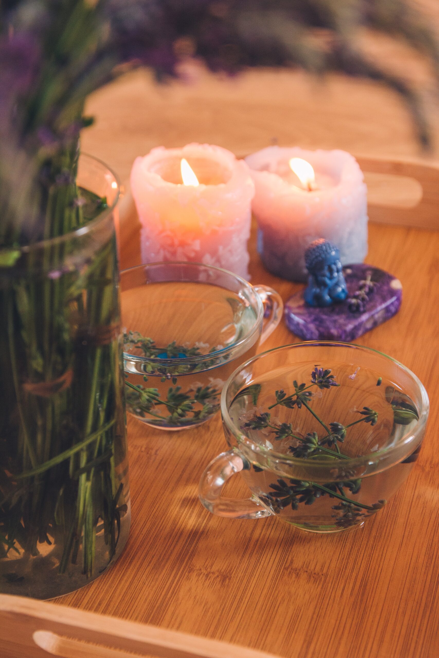 A photo of candles, cups of water with soaking herbs, and a stone sitting on a wooden tray.
